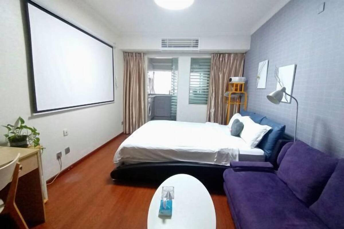Habitación de hotel con cama, sofá, escritorio y pantalla para proyector.