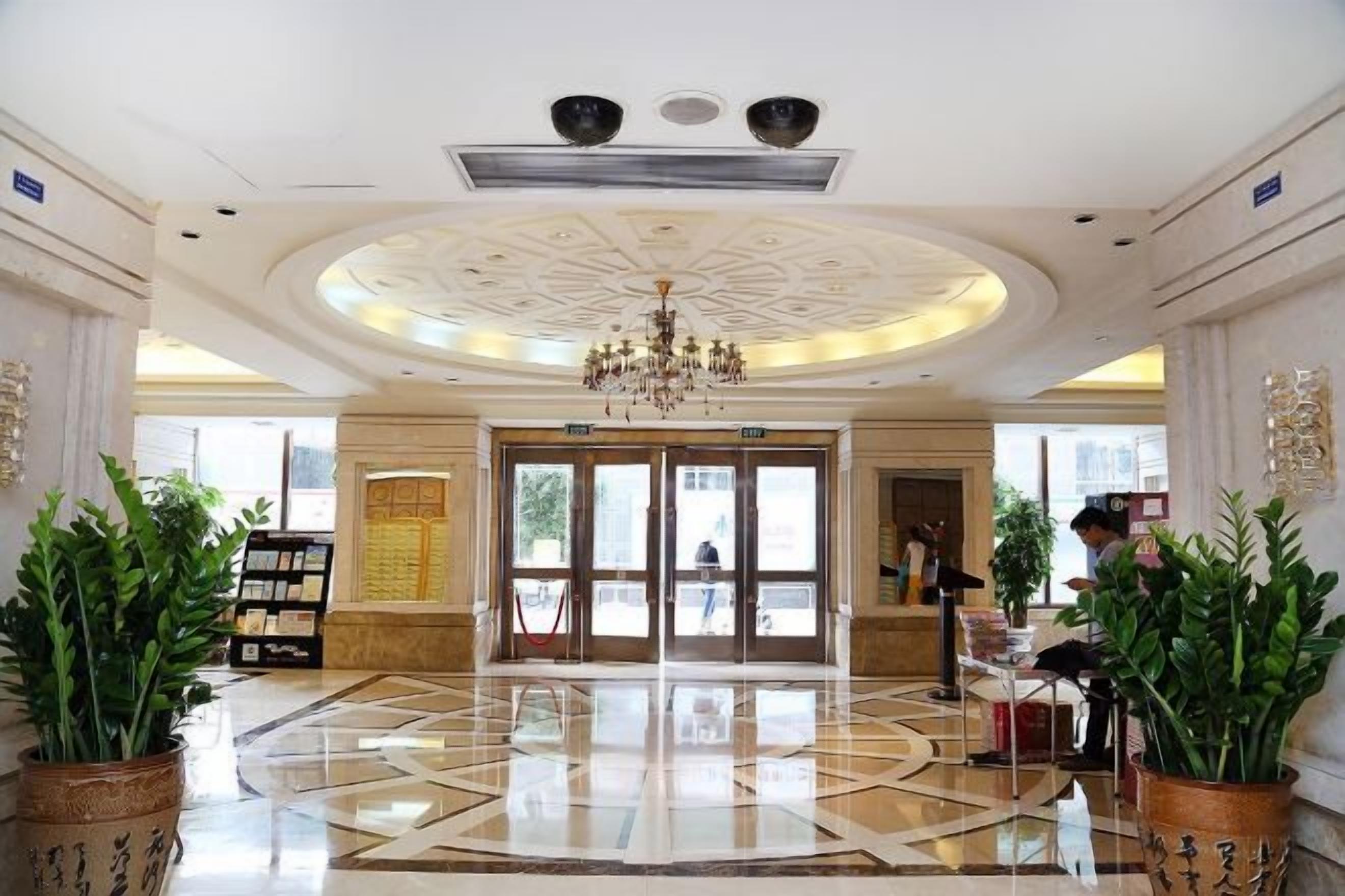 A hotel lobby with a chandelier, a reception desk, and potted plants.