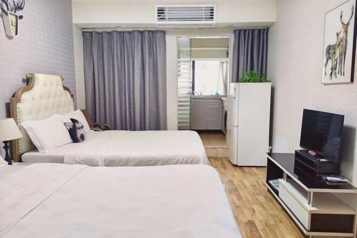 Habitación de hotel con dos camas, televisión, escritorio y baño visible a través de una puerta.