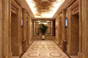 A hallway with marble walls and a patterned floor, leading to a reception area with a plant. - Shenzhen Life Home Apartment (Shenzhen Huaqiangbei Science Museum Subway Station) (Shenzhen)