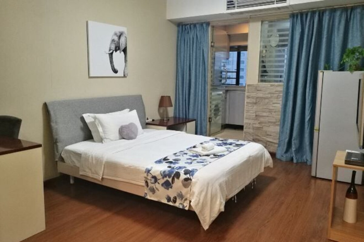 Un dormitorio con cama, escritorio, lámpara y vistas al exterior.
