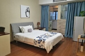 Un dormitorio con cama, escritorio, lámpara y vistas al exterior.