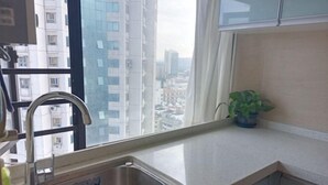 A kitchen with a stainless steel sink, a window with a view of tall buildings, and a potted plant on the counter. - Shenzhen Life Home Apartment (Shenzhen Huaqiangbei Science Museum Subway Station) (Shenzhen)