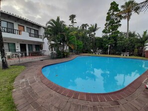 A swimming pool with a brick border, surrounded by palm trees and a building with balconies. - St Lucia Villa Mia 8 (St. Lucia)