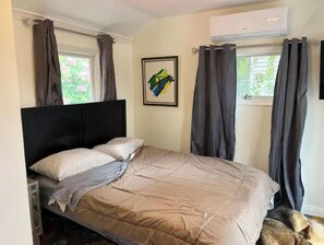 Cozy bedroom with a bed, headboard, and framed picture, featuring a window with curtains and air conditioning.