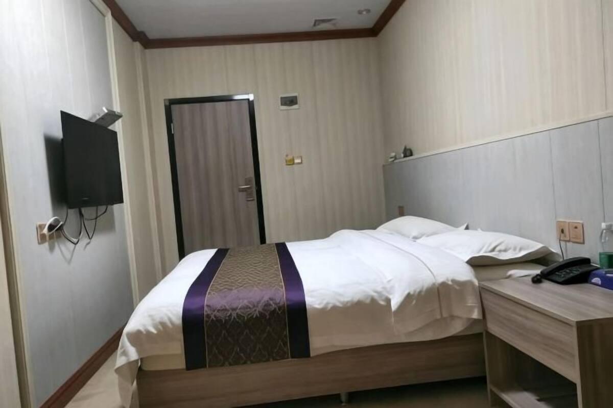 Hotellihuone, jossa on sänky, työpöytä, tuoli, seinälle asennettu televisio ja ovi.