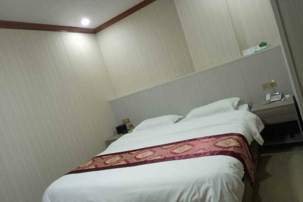 Hotellihuone, jossa on sänky, yöpöytä ja seinälle kiinnitetty hylly.