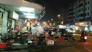 Una escena callejera con un puesto de comida, motocicletas y un edificio de varios pisos.