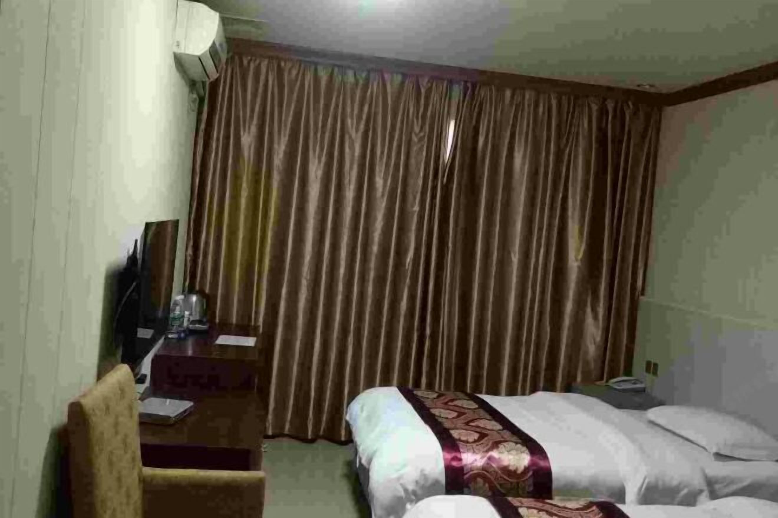 Quarto de hotel com uma cama, uma escrivaninha, uma cadeira, uma televisão e uma cortina.