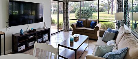 Una sala de estar moderna con un televisor de pantalla plana, un conjunto de sofá, una mesa de centro y un comedor.