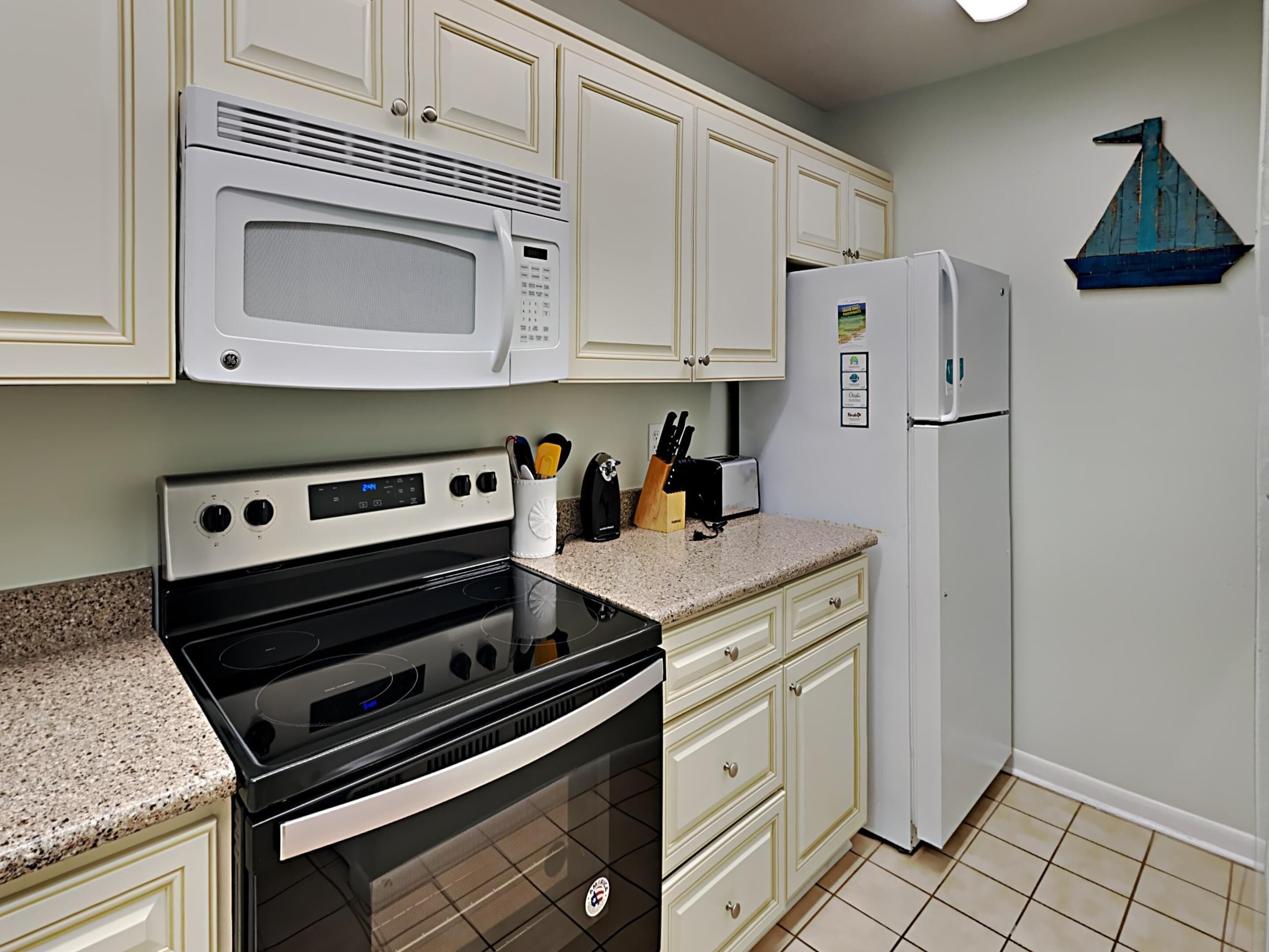 A kitchen with white cabinets, a microwave, a stove, a refrigerator, and a toaster.