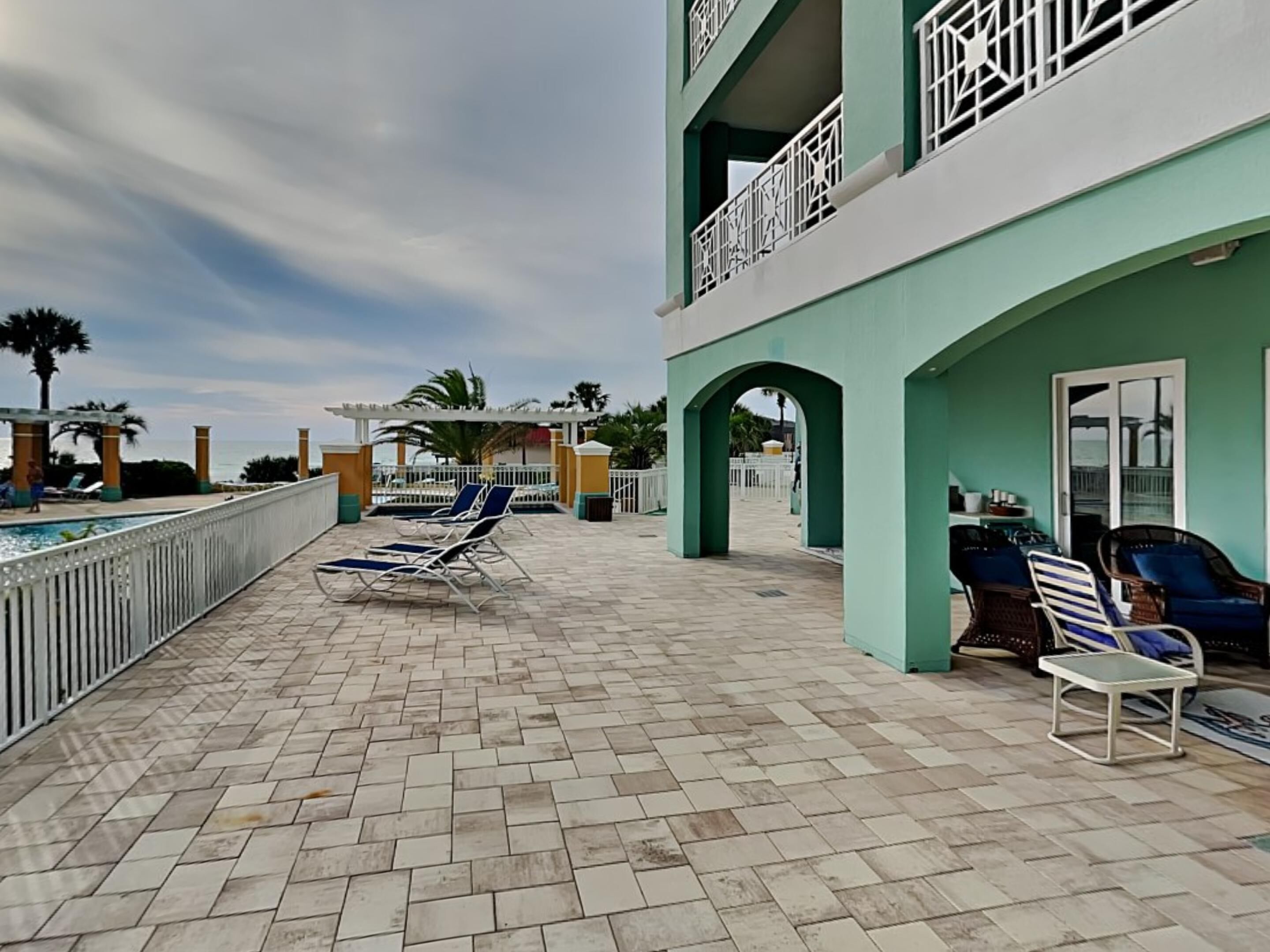 A poolside area with lounge chairs, a pergola, and a view of the sea.