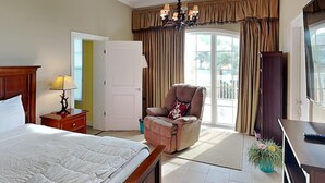Une chambre d’hôtel avec un lit, une chaise, un bureau, une lampe, un lustre, des rideaux et une vue sur l’extérieur.