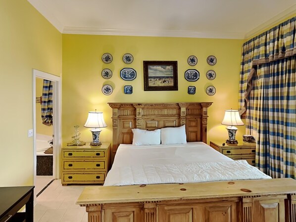 A bedroom with a wooden bed, two bedside tables with lamps, a dresser, and a wall decorated with blue and white plates.