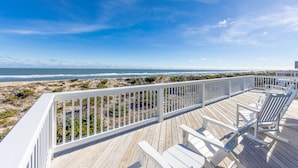 A wooden deck with white railings overlooking a beach.