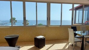 A balcony with a view of the ocean, wicker furniture, and a glass table.