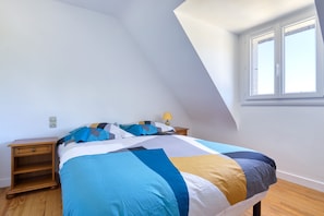 Una camera da letto con soffitto spiovente, un letto con copriletto multicolore, un comodino con lampada e una finestra con persiane.
