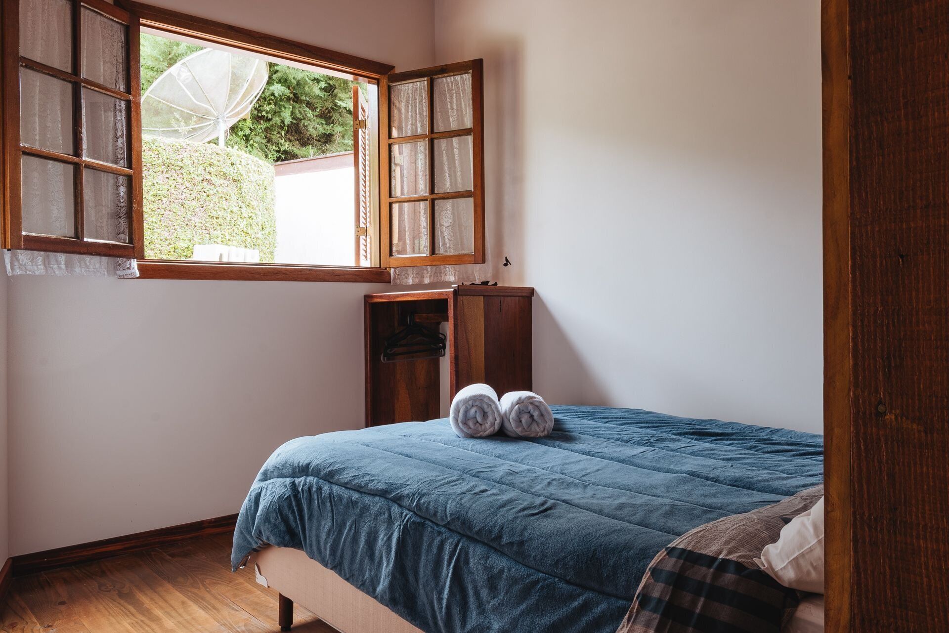 Une chambre à coucher avec un lit, une armoire en bois, une fenêtre avec des volets ouverts et une vue sur la verdure.