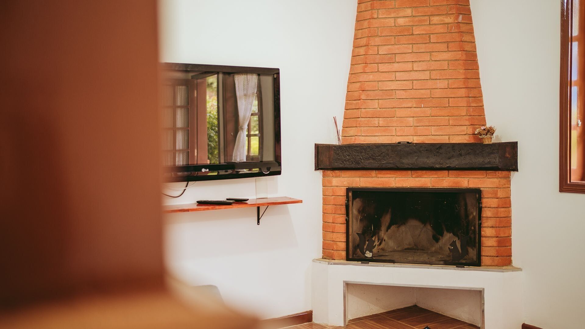 A living room with a brick fireplace, a mounted TV, and a wooden shelf.