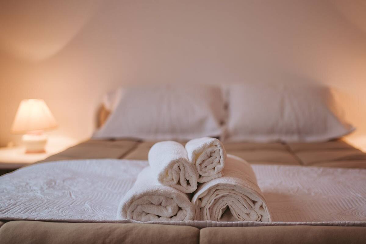 A neatly made bed with rolled towels, two bedside lamps, and a headboard.