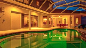 Une piscine à fond de verre, entourée d’un patio couvert comprenant une table et des chaises.