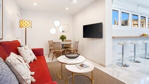 Ett modernt vardagsrum med en röd soffa, två runda bord, en tv och en matplats med stolar och en växt.