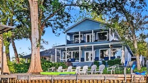 A waterfront house with a dock, outdoor seating, and a large tree.