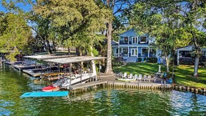 A waterfront property with a dock, boats, and a large blue house.