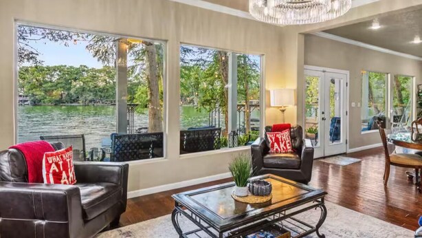 A spacious living room with large windows, a chandelier, and leather furniture.