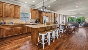 A spacious kitchen with wooden cabinets, a large island with stools, and a dining area with a table and chairs.