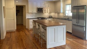 A modern kitchen with white cabinetry, a wooden island with bar stools, stainless steel appliances, and pendant lighting.