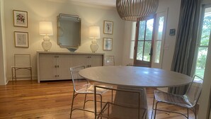 A dining area with a round table, clear chairs, a wooden floor, a cabinet with a mirror, and framed pictures on the wall.