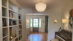 A spacious hallway with wooden flooring, a grand piano, and a bookshelf filled with books and decorative items.