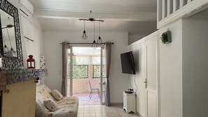 Een kamer met een bank, een aan de muur bevestigde televisie, een klein tafeltje en een glazen schuifdeur naar een buitenruimte.