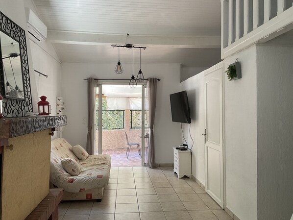 Una habitación con sofá, televisión montada en la pared, una mesita y un ventanal corredero que da a un espacio exterior.