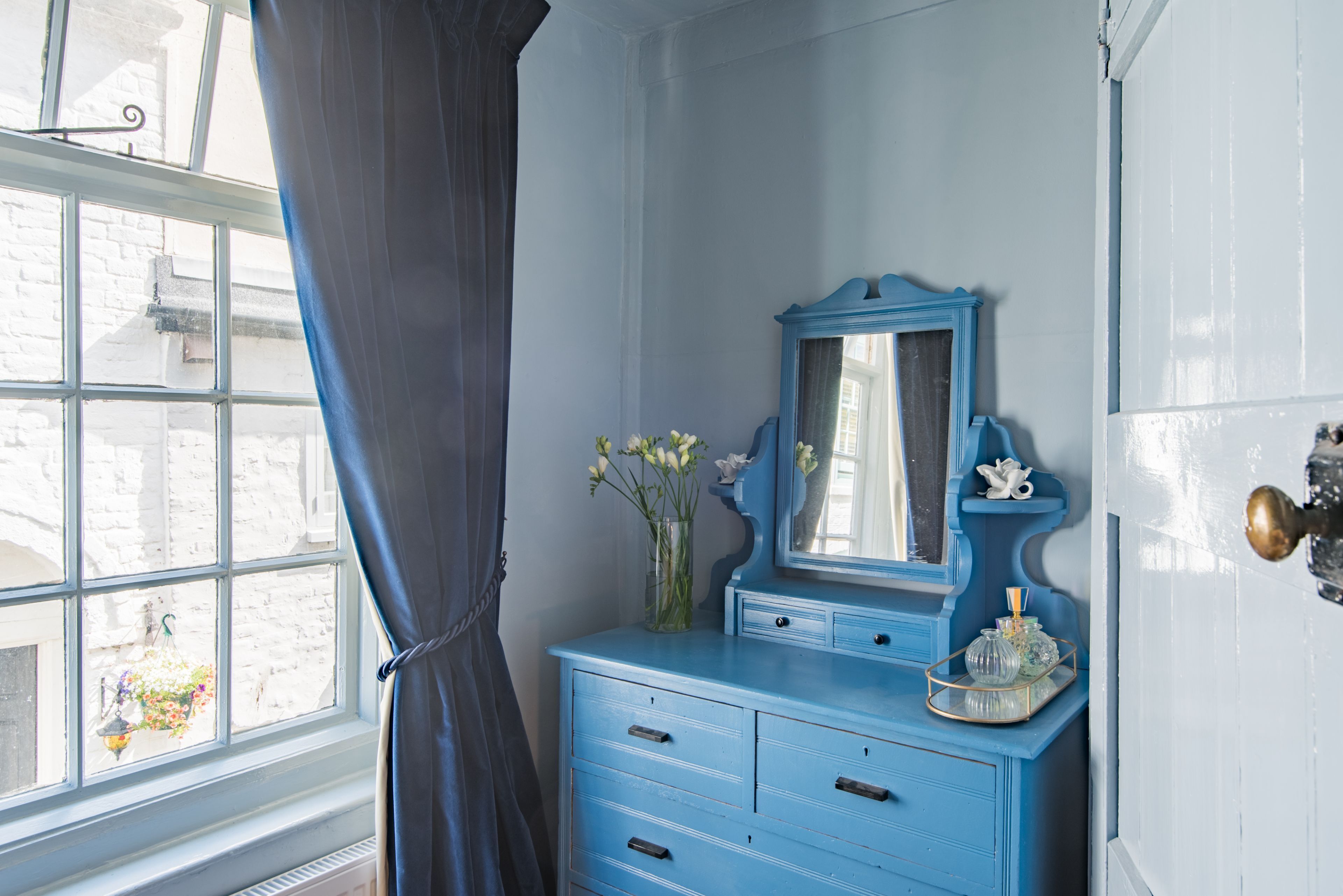 A room with a blue dresser, a mirror, and a window with curtains.