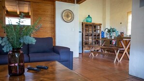 A living room with a dark blue sofa, a wooden coffee table, and a vase with green plants. There is a wooden cabinet with glass doors and a clock on the wall. - Cabañas La Serenisima (Tapalpa)