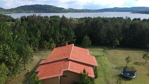 A house with a red-tiled roof surrounded by a grassy area and trees, with a lake and hills in the background. - Cabañas La Serenisima (Tapalpa)