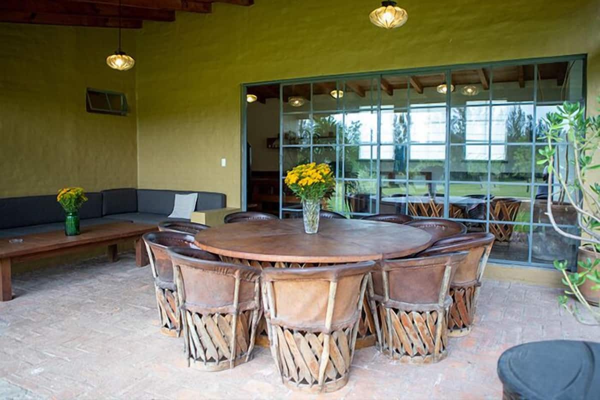 A round wooden table with six chairs, a bench, and a vase with yellow flowers.