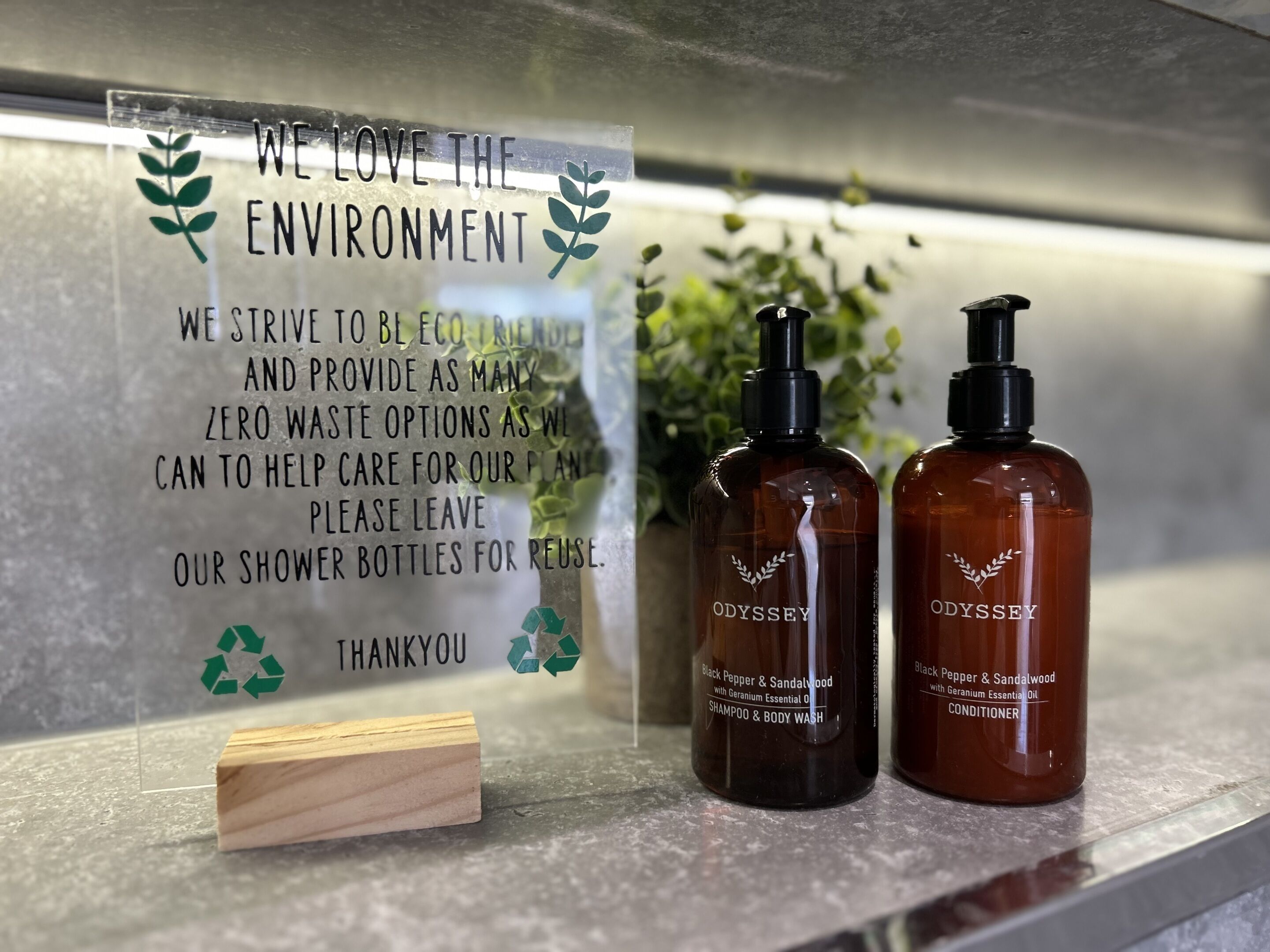A sign promoting eco-friendly practices and two bottles of Odyssey brand products on a countertop.