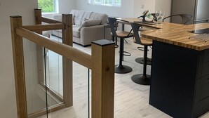 A modern kitchen with a wooden island, a dining area with a sofa, and a view of greenery outside. - Luxury Cottage, Views of the Lakes With Hot Tub (Cockermouth)