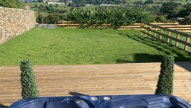 A hot tub on a wooden deck with a view of a green lawn and distant houses. - Luxury Cottage, Views of the Lakes With Hot Tub (Cockermouth)