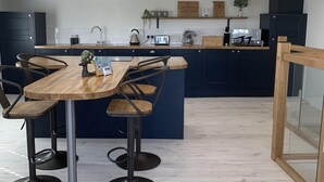 Une cuisine moderne dotée d’un îlot central, de meubles de rangement aux couleurs sombres et d’une table à manger en bois, accompagnée de tabourets de bar.