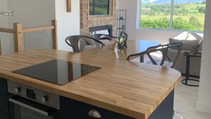 Une cuisine moderne dotée d’un îlot central, d’un four encastré et d’un coin repas offrant une vue sur la campagne.