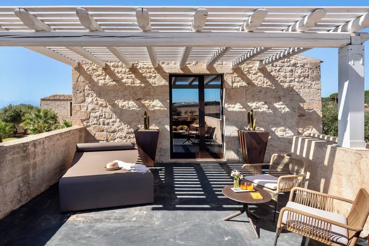 Une terrasse sur le toit agrémentée d’une pergola, de murs en pierre, de mobilier d’extérieur et de cactus en pot.