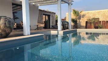 A clear blue pool with a pergola overhead, stone walls, and outdoor seating.
