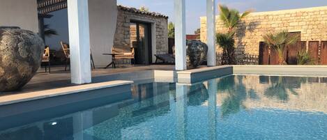Une piscine d’un bleu éclatant, surmontée d’une pergola, avec des murs en pierre et des espaces de détente en plein air.