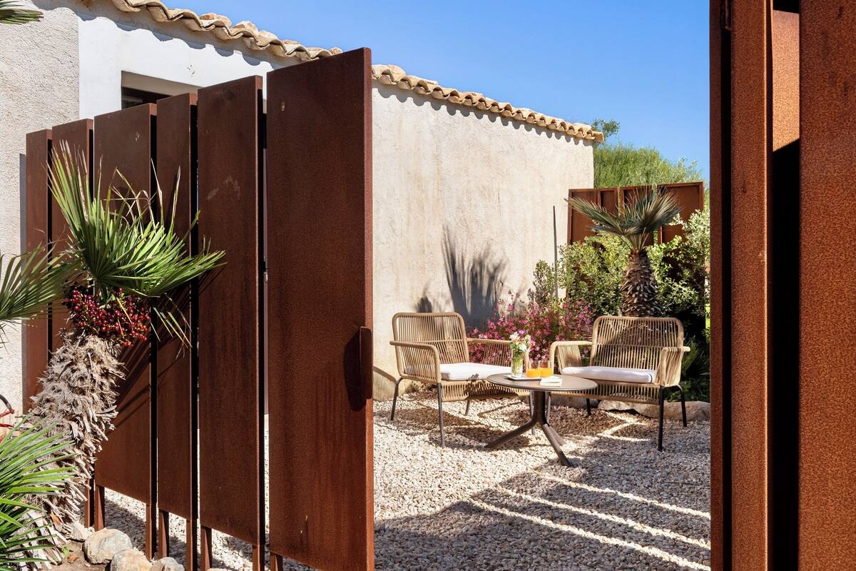 Une terrasse extérieure avec une table et des chaises, entourée d’une zone recouverte de gravier et de plantes.