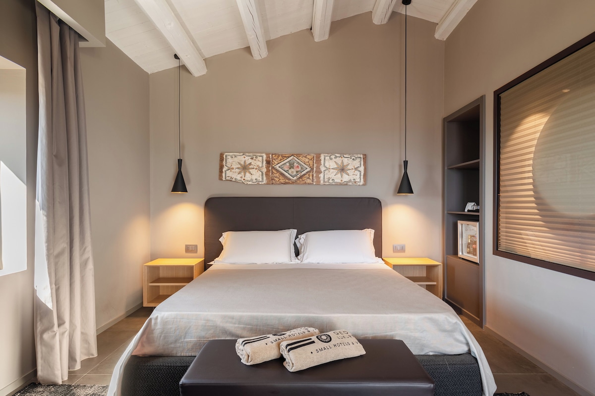 Ein modernes Schlafzimmer mit einem großen Bett, Nachttischen, einer Bank mit Handtüchern und dekorativer Wandkunst.