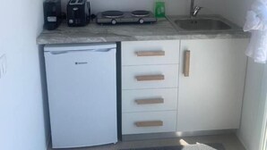 Cocina compacta equipada con lavavajillas, cafetera, hervidor y fregadero.